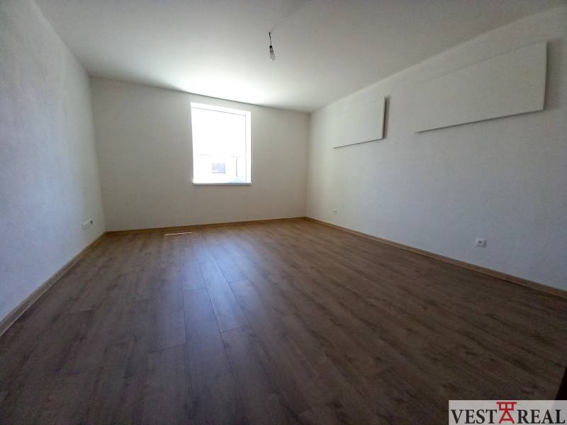 Ein Zimmer mit Holzboden und einem hellen Fenster in einem Einfamilienhaus.