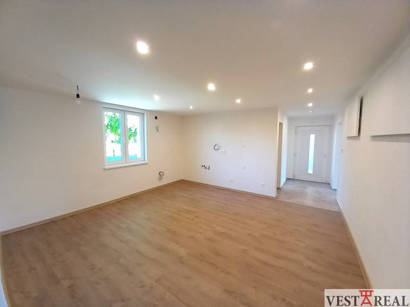 Geräumiges Wohnzimmer in einem Einfamilienhaus mit Holzboden und weißen Wänden.