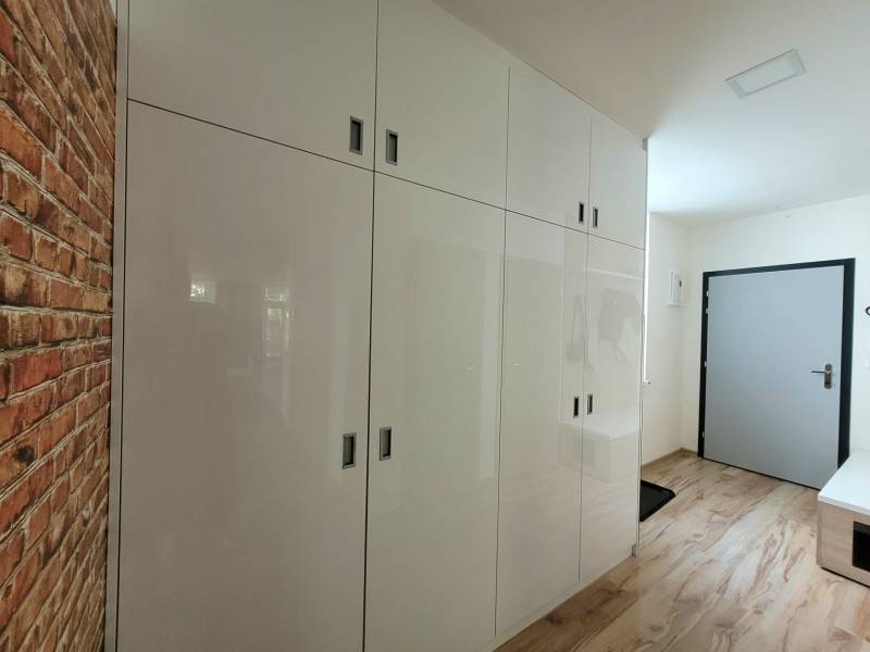 Eingangsflur in einer 3-Zimmer-Wohnung mit weißen Schränken und Ziegelverkleidung.