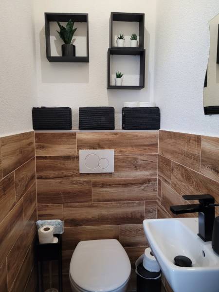Toilette in einer 3-Zimmer-Wohnung mit Holzverkleidung und schwarzen Accessoires.