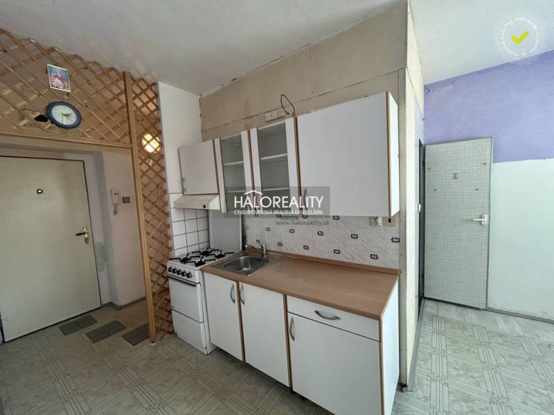 Küche in einer Einzimmerwohnung mit Gasherd und Schränken an der weißen Wand.
