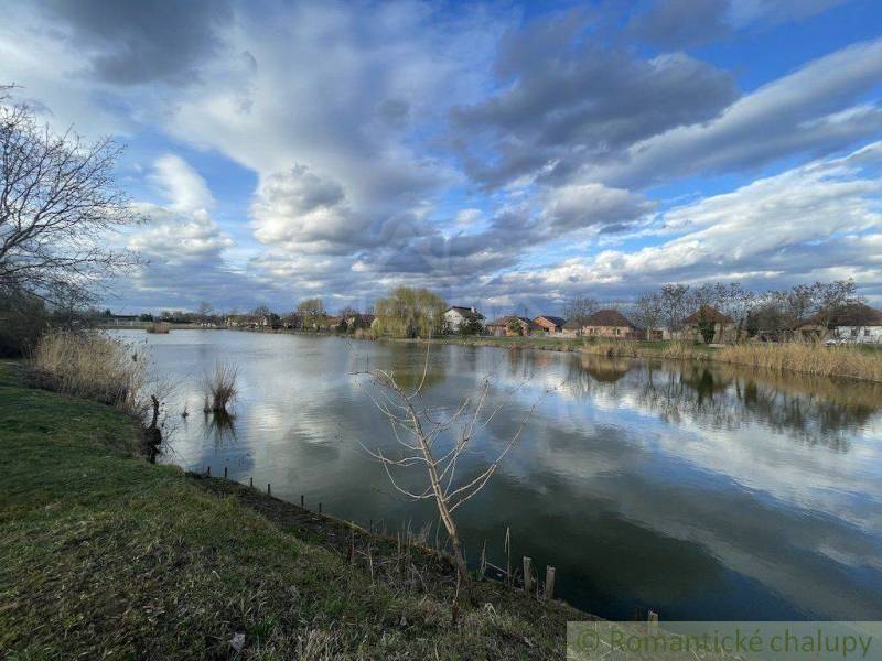 Idyllische Landschaft mit einem See, Wolken und Einfamilienhäusern im Hintergrund am Ufer.