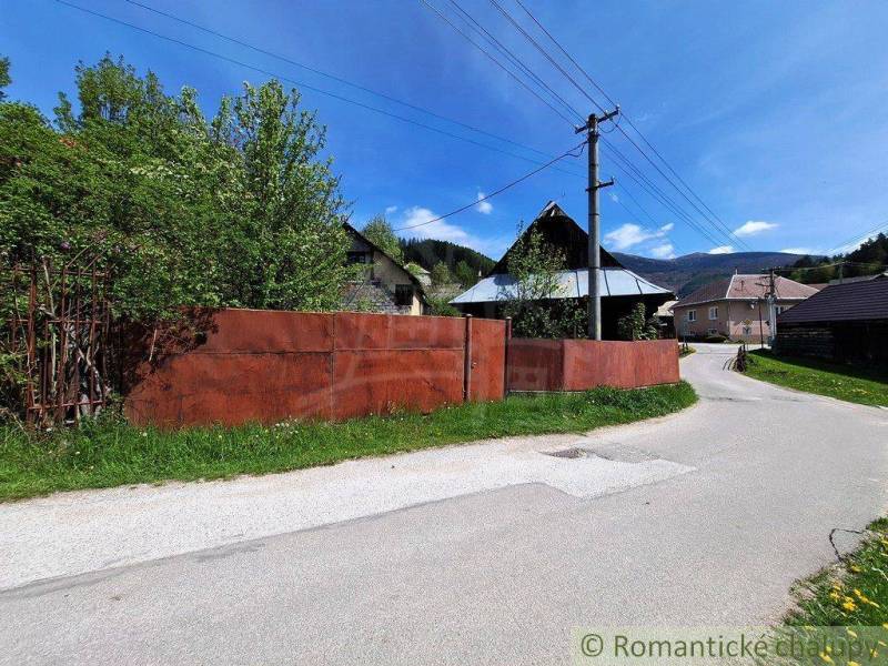 Ein Einfamilienhaus in Pohorelá mit Garten, einem Blechzaun und Strommasten an der Straße.