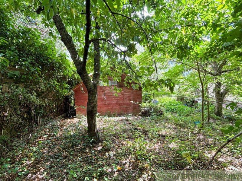 Ein Garten in Malacky mit einem roten Häuschen, umgeben von Bäumen und üppigem Grün.