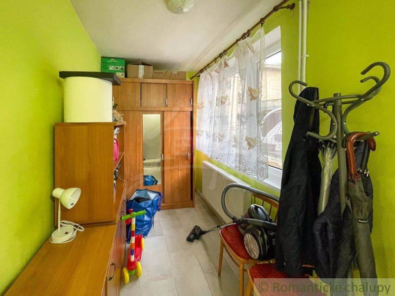 Ein Flur in einem Einfamilienhaus mit Möbeln, einem Kleiderständer und einem Fenster mit Blumenvorhängen.