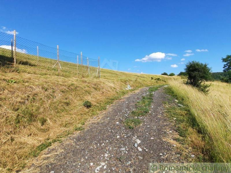 Ein Feldweg in den Gärten in Žarnovica, umgeben von grasbewachsenen Hängen und einem Zaun.