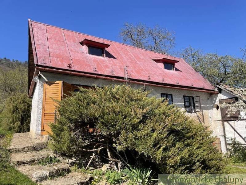 Ein Ferienhaus in Rožňava mit rotem Dach, umgeben von üppigem Grün und klarem Himmel.