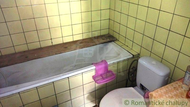 Ein Badezimmer in einem Einfamilienhaus mit einer Badewanne und einer Toilette, umgeben von gelben Fliesen.