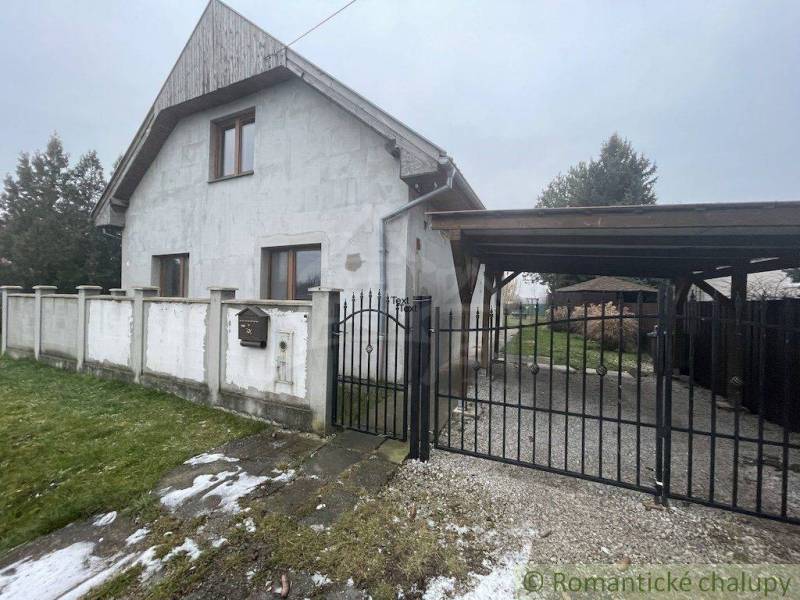 Ein Einfamilienhaus mit weißer Fassade und Tor, umgeben von Rasen und Zaun.