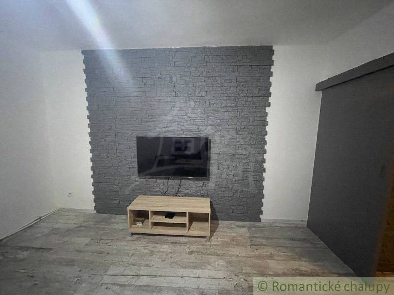 Fernseher an der Steinwand, darunter ein Holztisch, Raum in einem Einfamilienhaus.