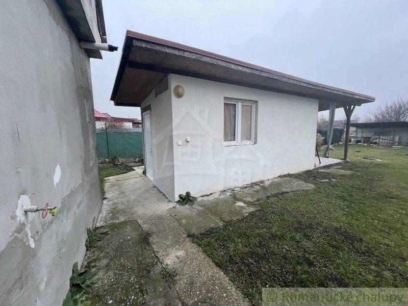 Ein Gartenpavillon bei einem Einfamilienhaus auf einer befestigten Fläche mit Rasen und Zaun.