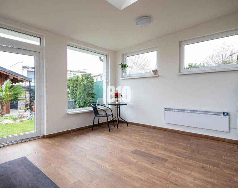 Innenraum eines Einfamilienhauses mit Holzboden, Tisch und Stühlen bei großen Fenstern.