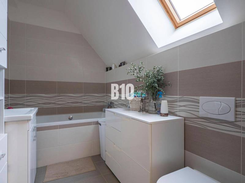 Ein Badezimmer in einem Einfamilienhaus mit einer Badewanne, hellen Fliesen und einem Dachfenster.