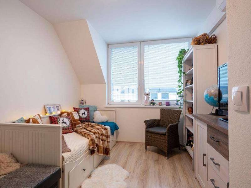 Kinderzimmer in einem Einfamilienhaus mit Bett, Sessel, Regalen und Fenster.