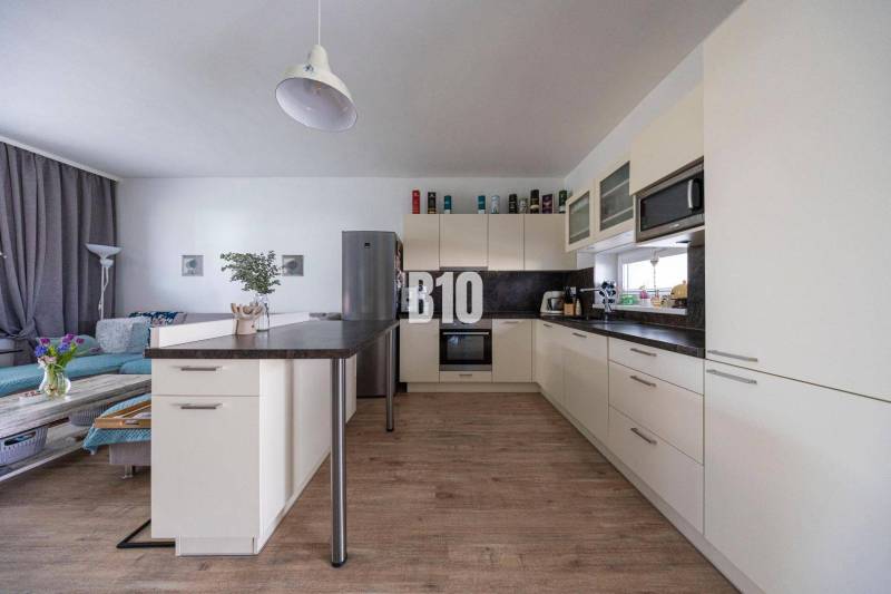 Küche mit Insel und bequemer Sitzgelegenheit in einem Einfamilienhaus, helle Putzwände und Holzboden.