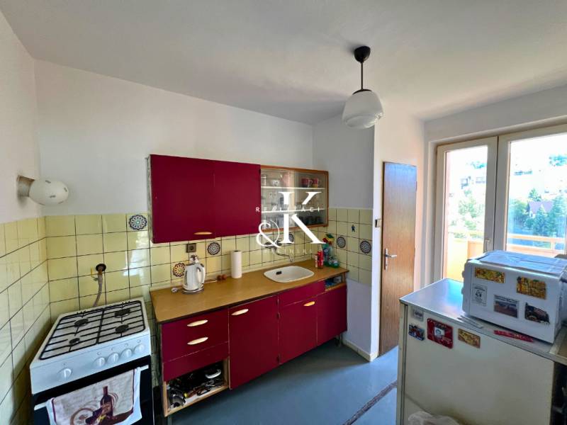 Küche einer 2-Zimmer-Wohnung mit roten Schränken und einem älteren Gasherd.