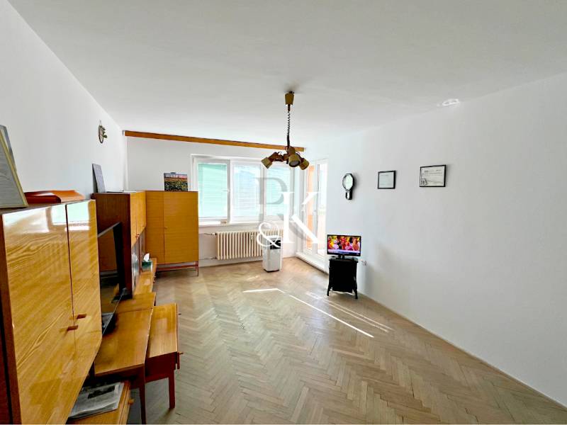 Wohnzimmer in einer Zweizimmerwohnung mit Holzmöbeln und einem Fernseher auf einem Ständer.