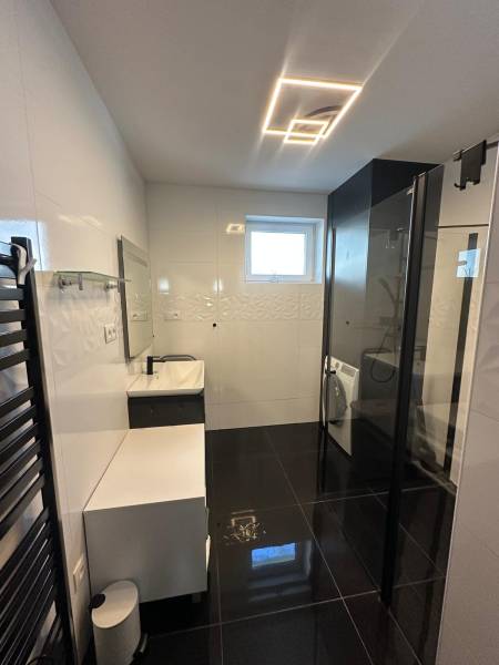 Ein Badezimmer in einem Einfamilienhaus mit schwarzen Böden, weißen Wänden und einer Duschkabine.