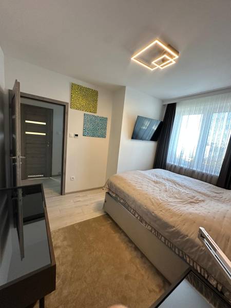 Ein Schlafzimmer in einem Einfamilienhaus mit Licht, Fernseher, Bildern und einem großen Fenster.