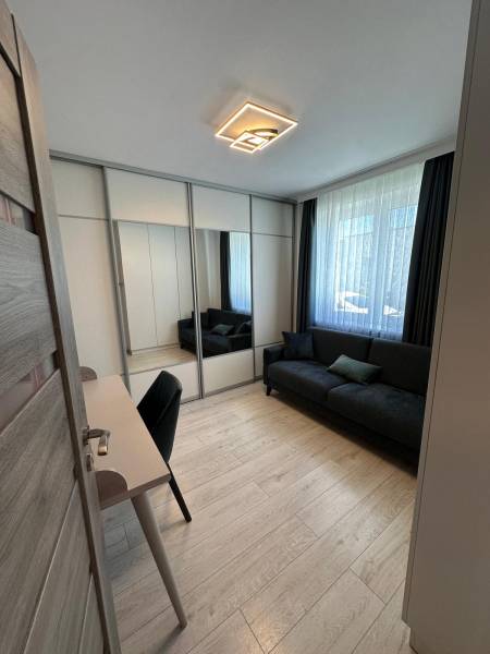 Ein Zimmer in einem Einfamilienhaus mit einem schwarzen Sofa, einem Schreibtisch und einem Spiegelschrank.