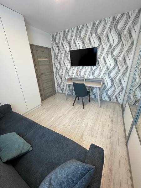 Ein Zimmer in einem Einfamilienhaus mit wellenförmiger Tapete, Fernseher, Sofa und Schreibtisch.