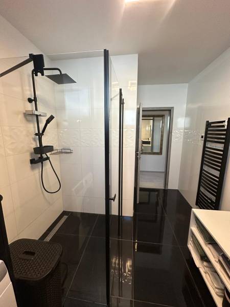 Badezimmer mit Dusche, schwarzen Fliesen und Stauraum in einem Einfamilienhaus.