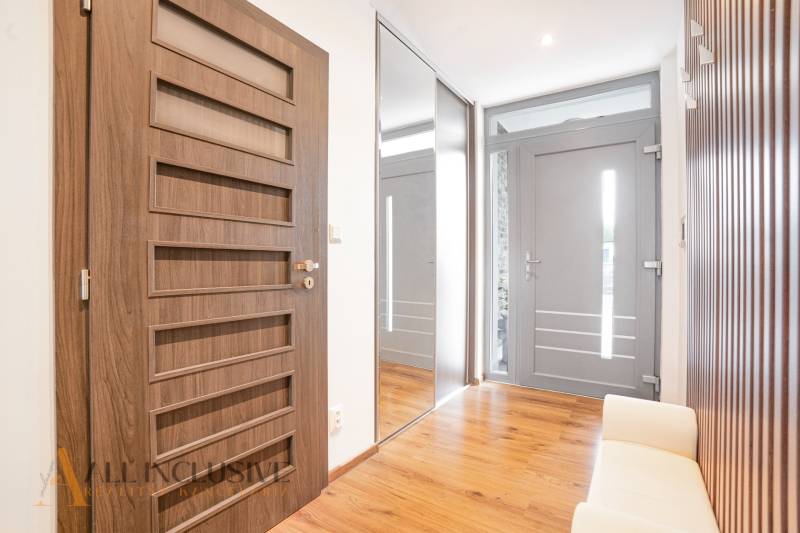 Ein Flur in einem Einfamilienhaus mit Holzboden, Spiegel und Türen mit geometrischen Elementen.
