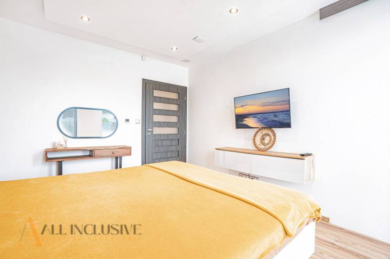 Helles Schlafzimmer in einem Einfamilienhaus mit Fernseher, Spiegel und gelber Bettdecke.