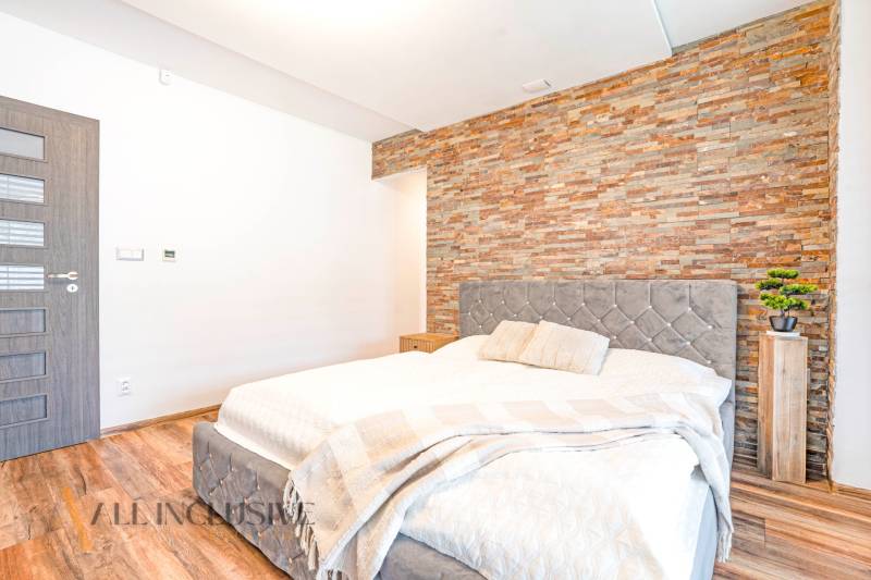 Ein Schlafzimmer in einem Einfamilienhaus mit einer Steinwand, einem eleganten Bett und dekorativen Accessoires.