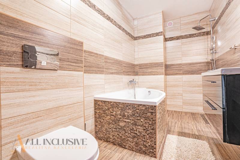 Badezimmer in einem Einfamilienhaus mit Badewanne, Dusche und Waschbecken, umgeben von beigen Fliesen.