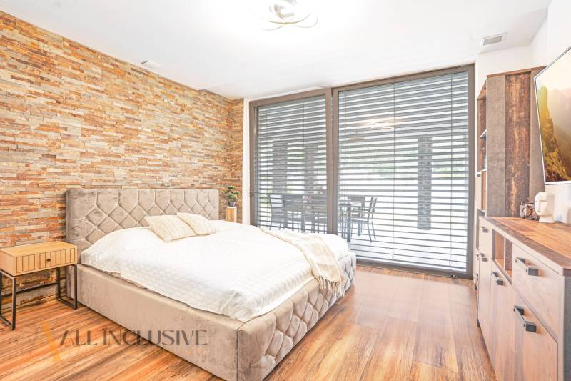 Schlafzimmer mit Steinwand, bequemem Bett und erweitertem Ausblick durch das Fenster in einem Einfamilienhaus.