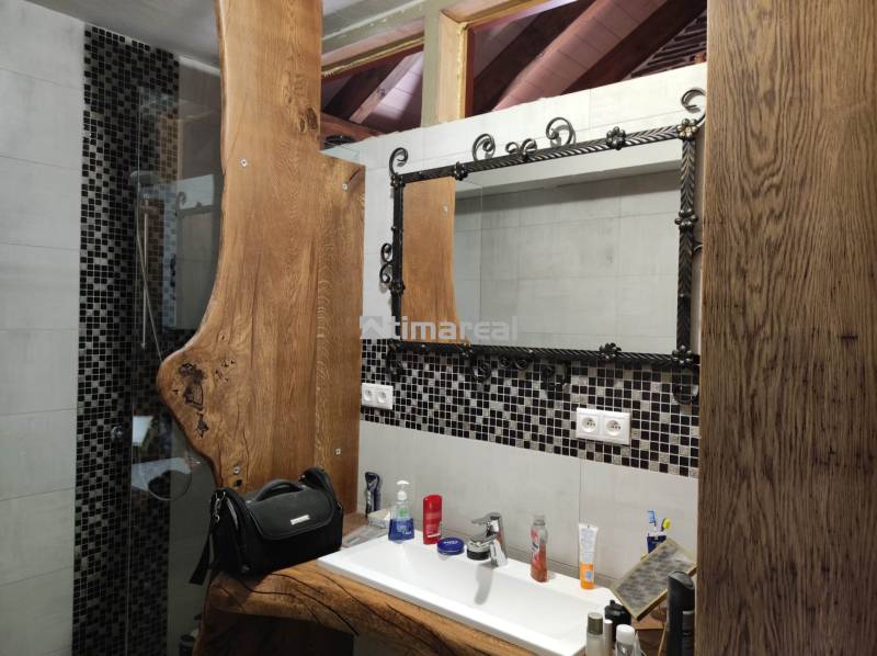 Badezimmer in einer 2-Zimmer-Wohnung mit einem Waschtisch aus Holz und einem Spiegel mit Metallrahmen.