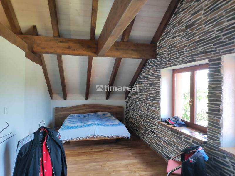 Dachbodenschlafzimmer mit Holzbalken, Steinverkleidung und Bett in einer Zweizimmerwohnung.
