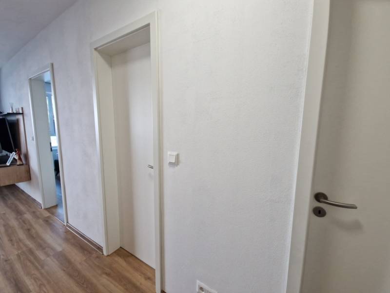 Flur in einer 2-Zimmer-Wohnung, weiße Türen und Holzboden, moderne Möbel im Hintergrund.