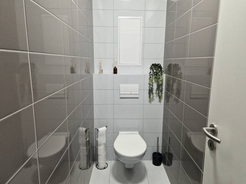 Badezimmer mit Toilette in einer 2-Zimmer-Wohnung, mit dunkelgrauen Fliesen an den Wänden.