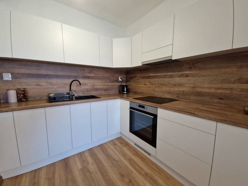 Weiße Küche in einer 2-Zimmer-Wohnung mit Holzarbeitsplatte und Holzboden.