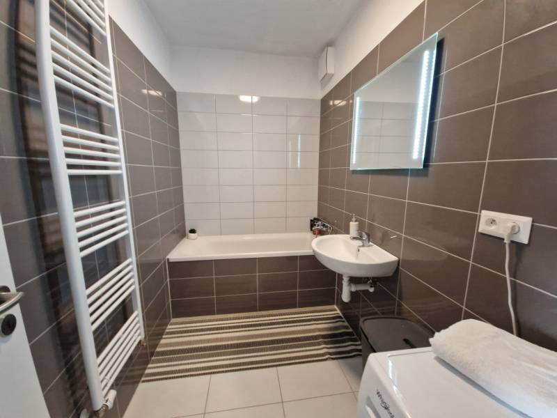 Ein Badezimmer in einer 2-Zimmer-Wohnung mit einer Badewanne, einem Waschbecken, einem Spiegel und einem Handtuchheizkörper.