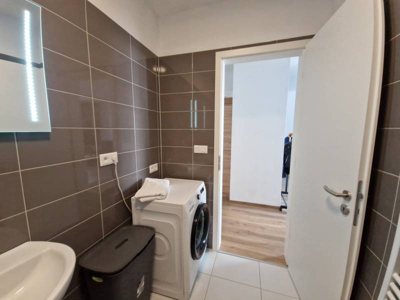 Badezimmer mit Spiegel, Waschbecken, Waschmaschine und Wäschekorb in einer 2-Zimmer-Wohnung.