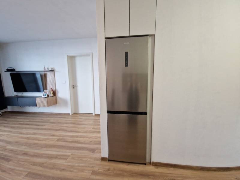 In der 2-Zimmer-Wohnung sieht man den Küchenbereich mit Kühlschrank und den Wohnbereich mit Fernseher.
