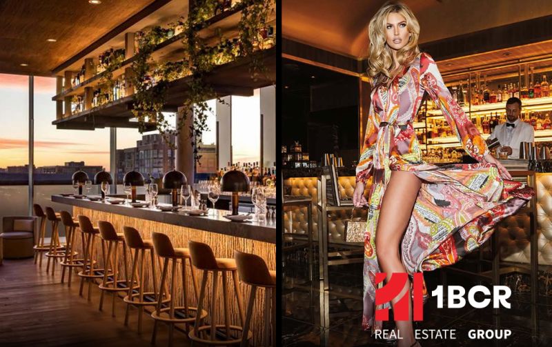 Ein stilvolles Bar-Interieur und ein Model in einem bunten Kleid an der Bar.