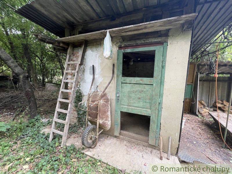 Ein baufälliger Schuppen mit Holztüren und einer Leiter auf dem Grundstück eines Einfamilienhauses in Branč.