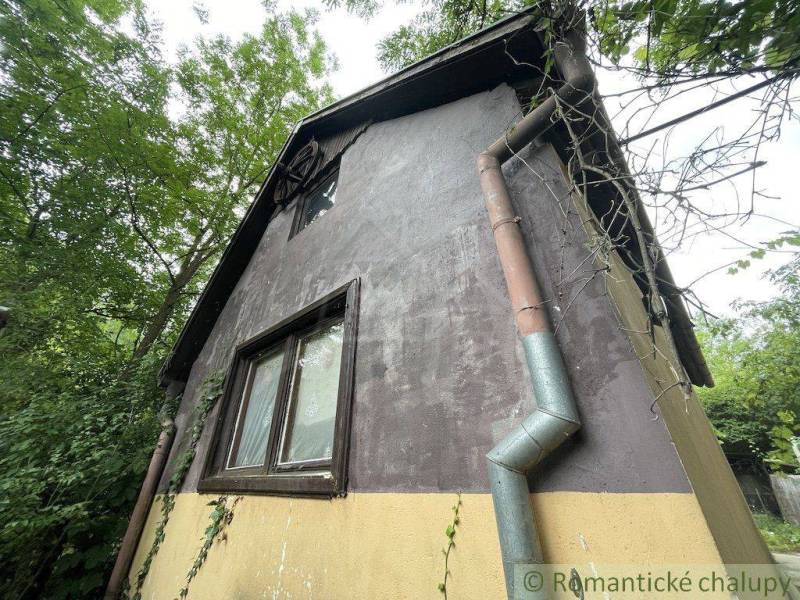 Ein Einfamilienhaus in Branč mit Putz, Kletterpflanzen und Holzfenstern.