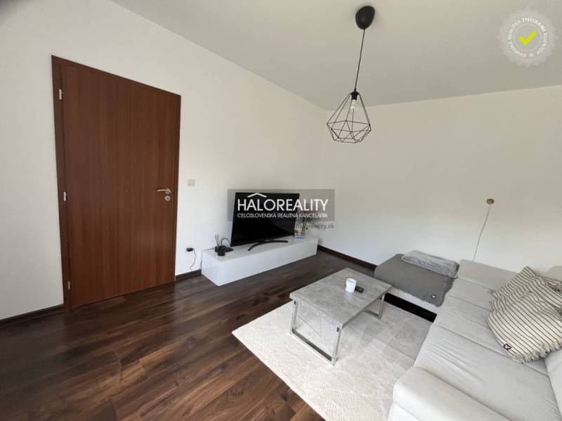 Wohnzimmer in einem Einfamilienhaus mit dunklem Boden, weißem Sofa und TV-Tisch.