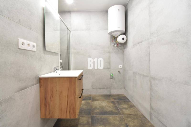 Badezimmer in einer 3-Zimmer-Wohnung mit Waschbecken und Boiler, helle Fliesen dominieren den Raum.