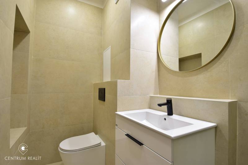 Badezimmer in einer 2-Zimmer-Wohnung mit Toilette, Waschbecken, schwarzem Wasserhahn und rundem Spiegel.