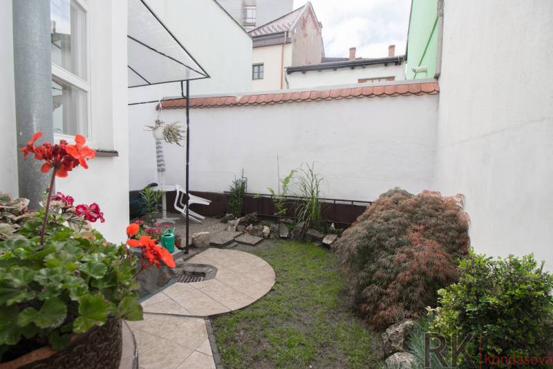 Ein kleiner Garten bei einer 2-Zimmer-Wohnung mit Pflastersteinen, Pflanzen und Steindekoration.