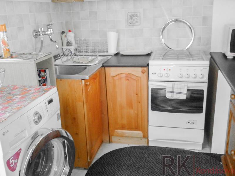 Küche in einer 2-Zimmer-Wohnung mit Waschmaschine, Herd und Holzschränken.