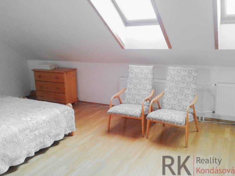 Dachzimmer mit zwei Sesseln, einer Kommode und einem Bett in einer Zweizimmerwohnung.