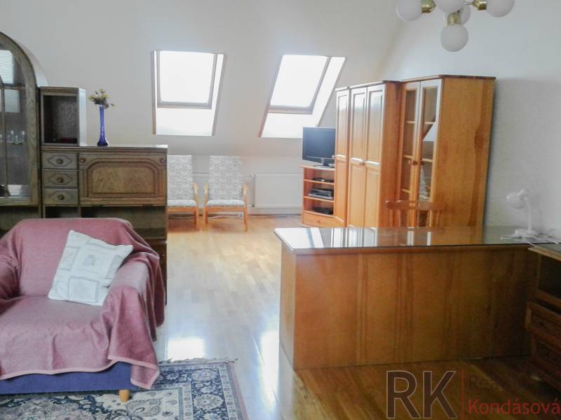 Dachgeschoss-Wohnzimmer mit Holzmöbeln und Dachfenstern in einer Zweizimmerwohnung.