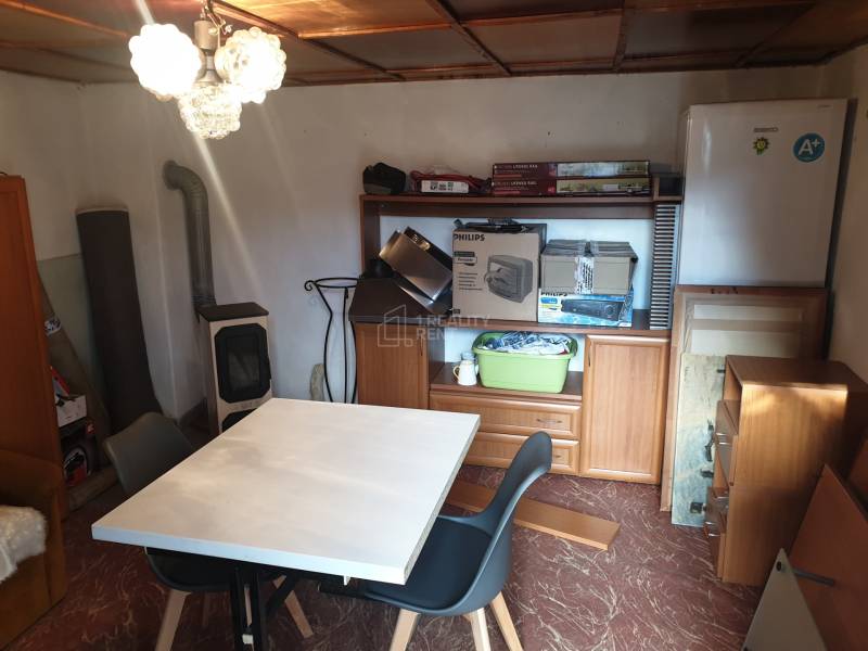 Kleiner Tisch, Stühle, Kleiderschrank, Kühlschrank, Kamin, Regale mit Gegenständen.